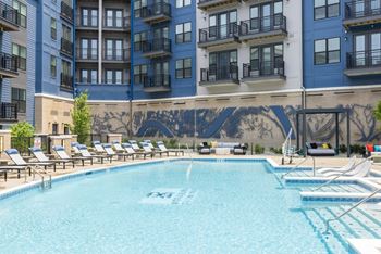 A large pool with lounge chairs in front of an apartment building